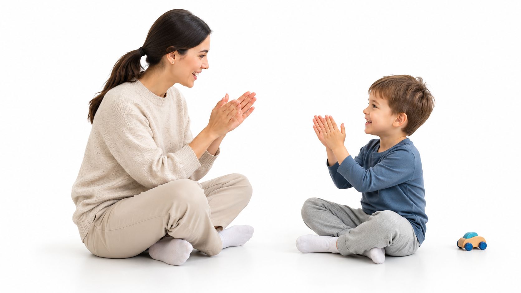 A mother and her young son sitting on a floor and playing a clapping game together