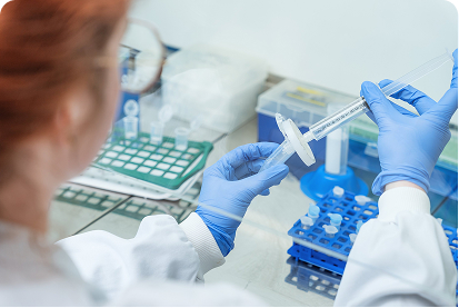 Scientist wearing blue gloves draws liquid from a vial using a syringe in a lab setting.
