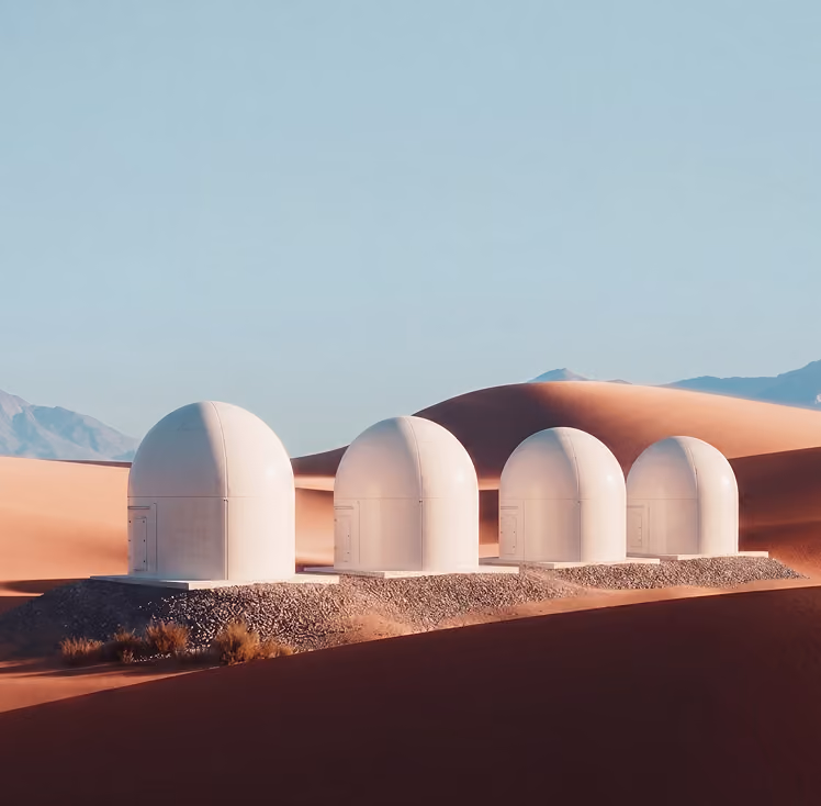 Four white dome-shaped observatories in a desert with sand dunes and mountains in the background.