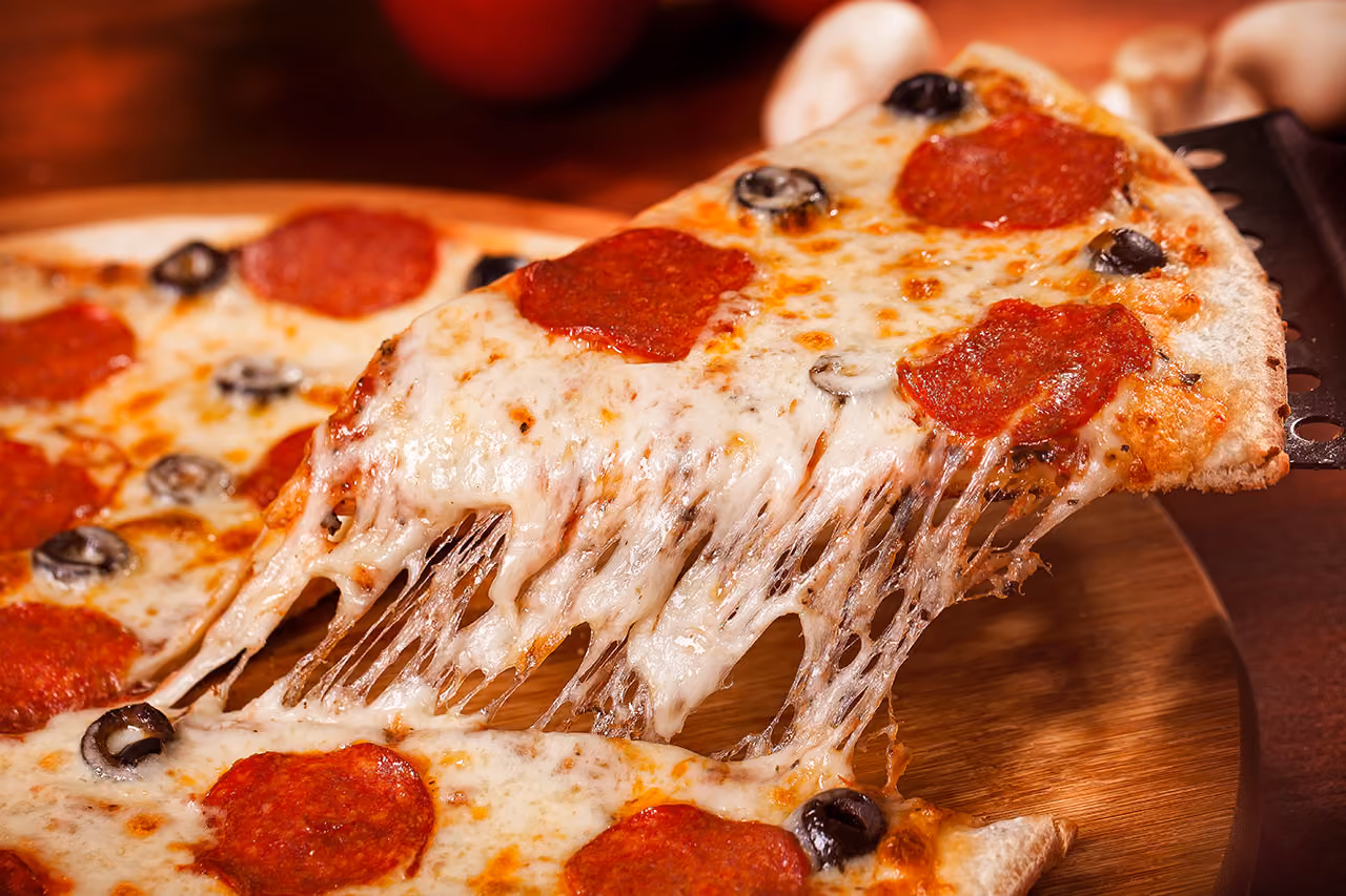 Slice of pepperoni pizza with melted cheese stretching as it is lifted from the whole pizza.