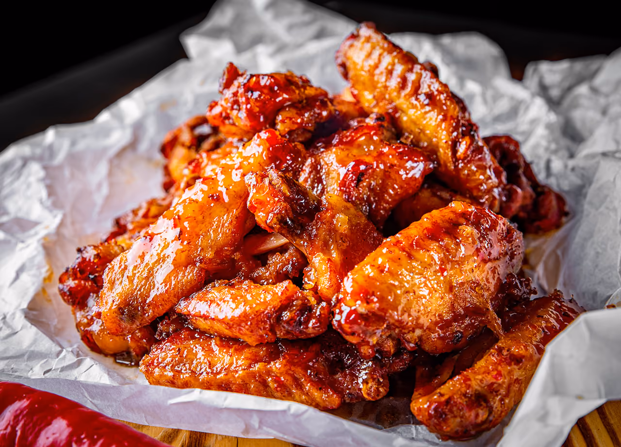 Pile of glazed chicken wings on crumpled white paper on wooden surface.