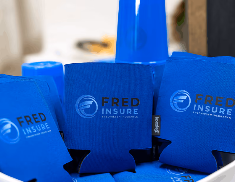 Blue beverage koozies with Fred Insure logo stacked with blue plastic cups in background.