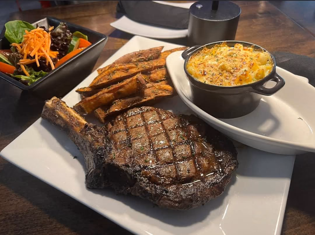 Grilled ribeye steak with seasoned potato wedges, macaroni and cheese, and a side salad.