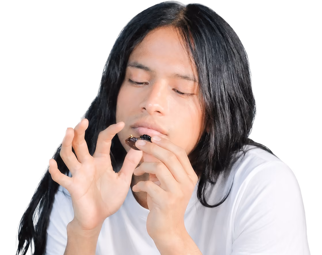 Person with long black hair wearing a white shirt, closely examining a small dark object held between their fingers.