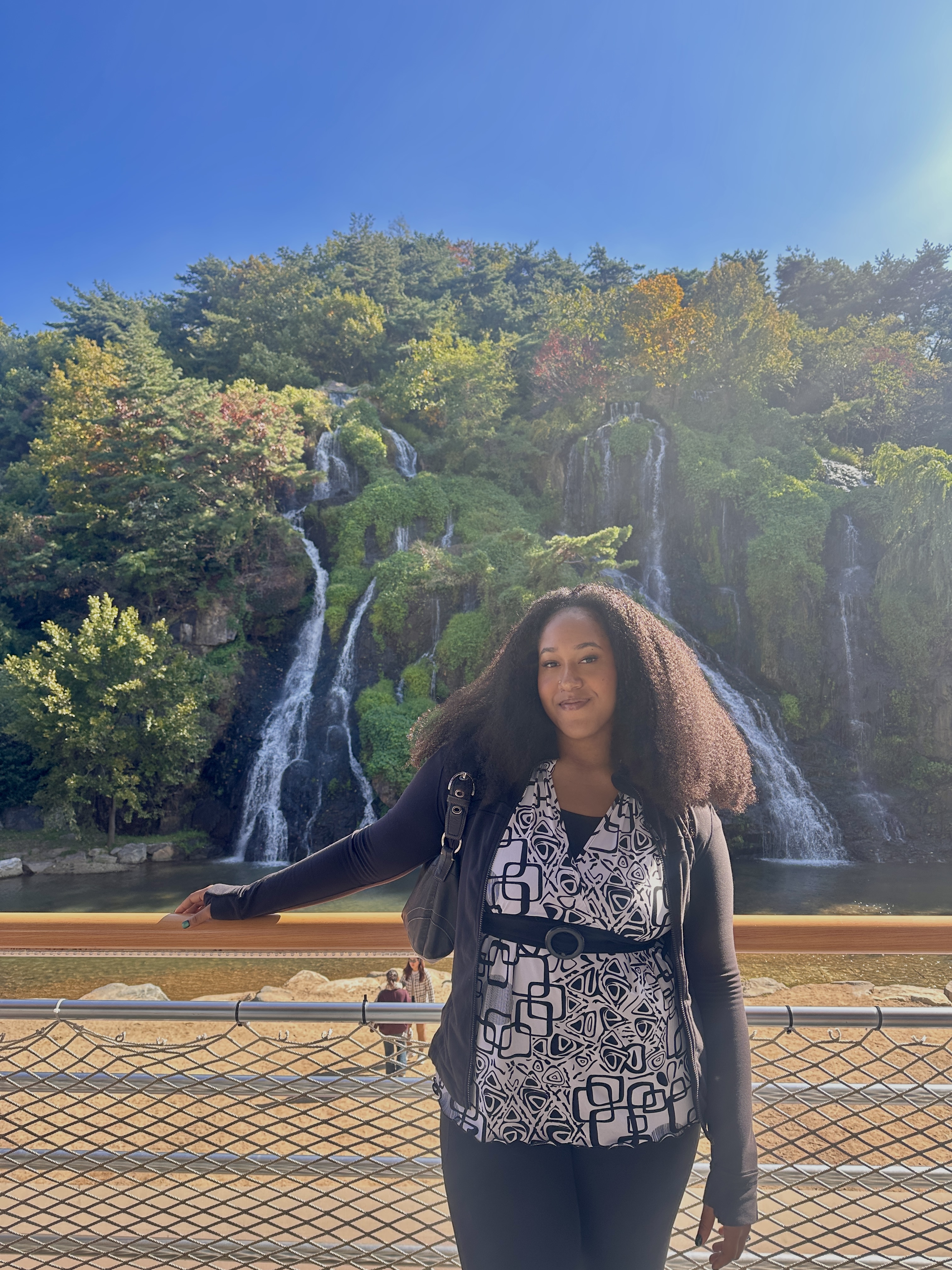 Rea standing in front of a waterfall and autumn trees