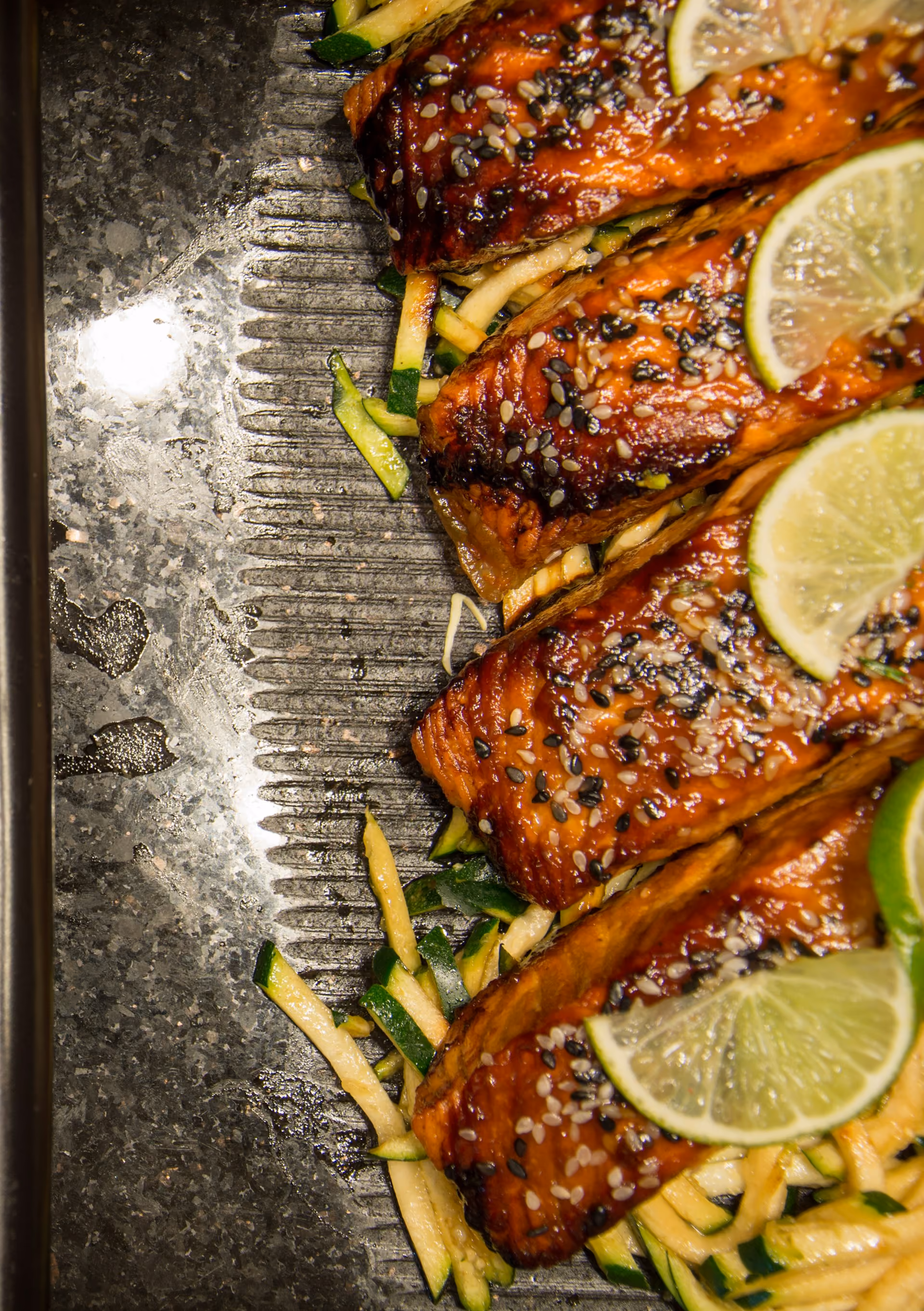 Grilled salmon fillets topped with sesame seeds and lime slices on a bed of julienned zucchini.