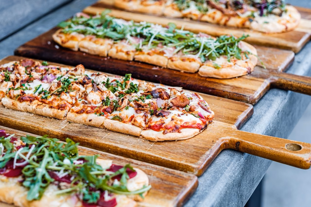 Three rectangular pizzas with varied toppings on wooden paddle boards on a table.