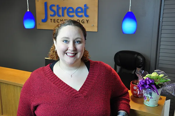 A smiling J Street Technology team member in front of the company sign at the office