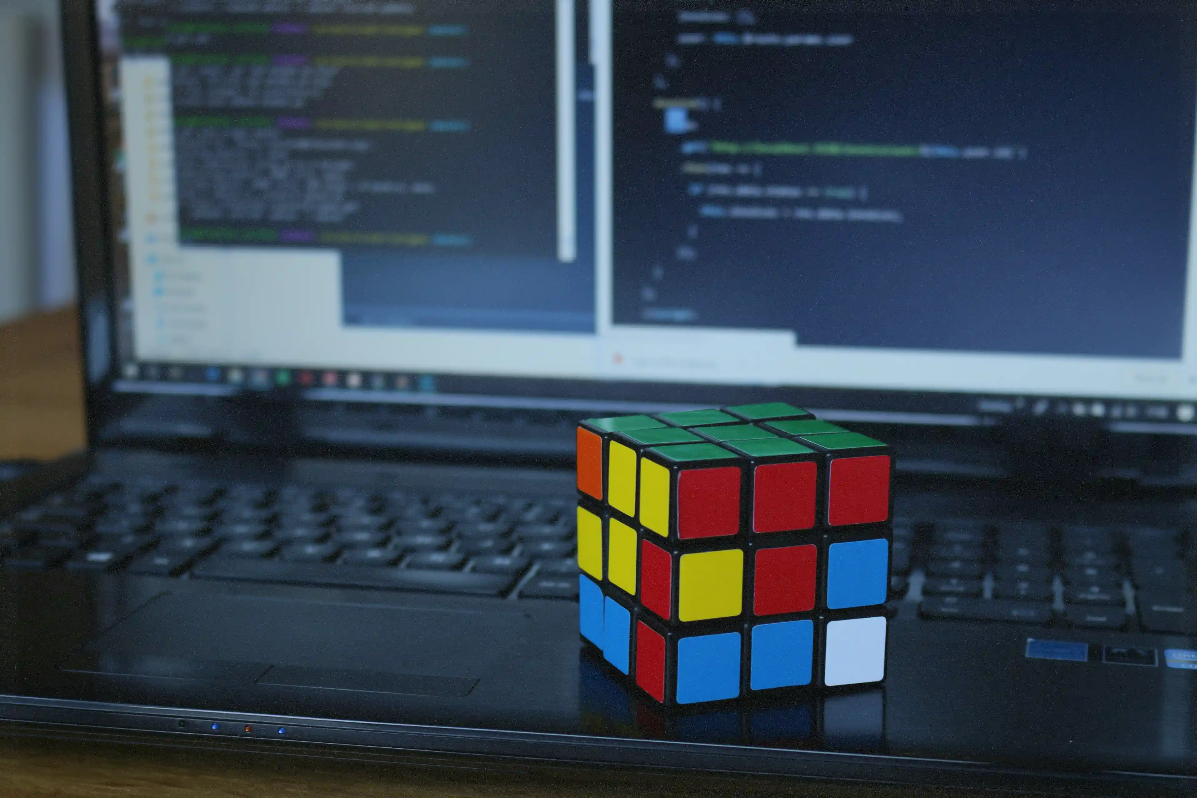 A colorful Rubik’s Cube resting on a laptop keyboard in front of code on screen