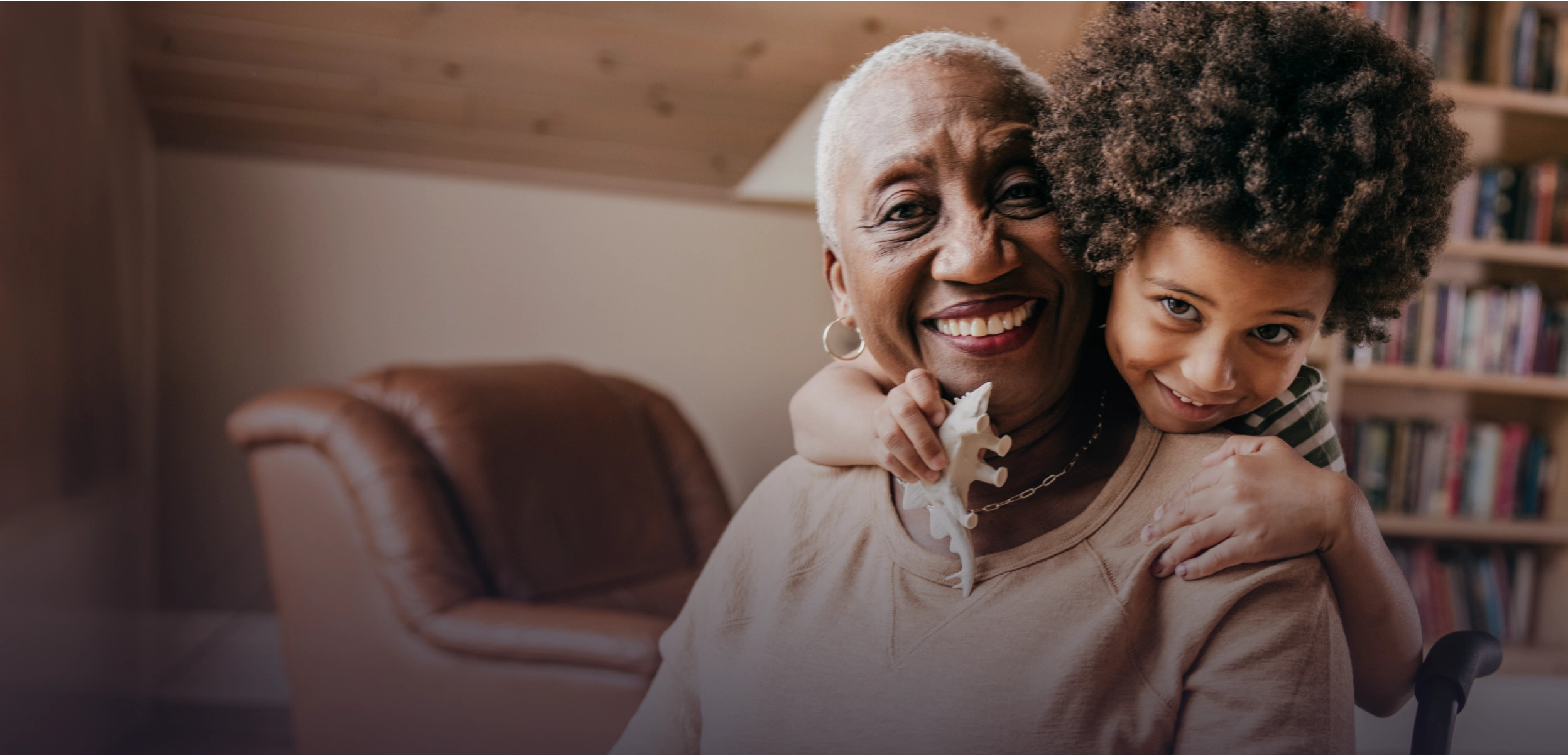 Grandmother smiling as her grandchild hugs her from behind