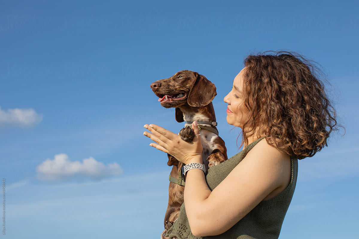Woman lifting her dog outdoors under a clear blue sky