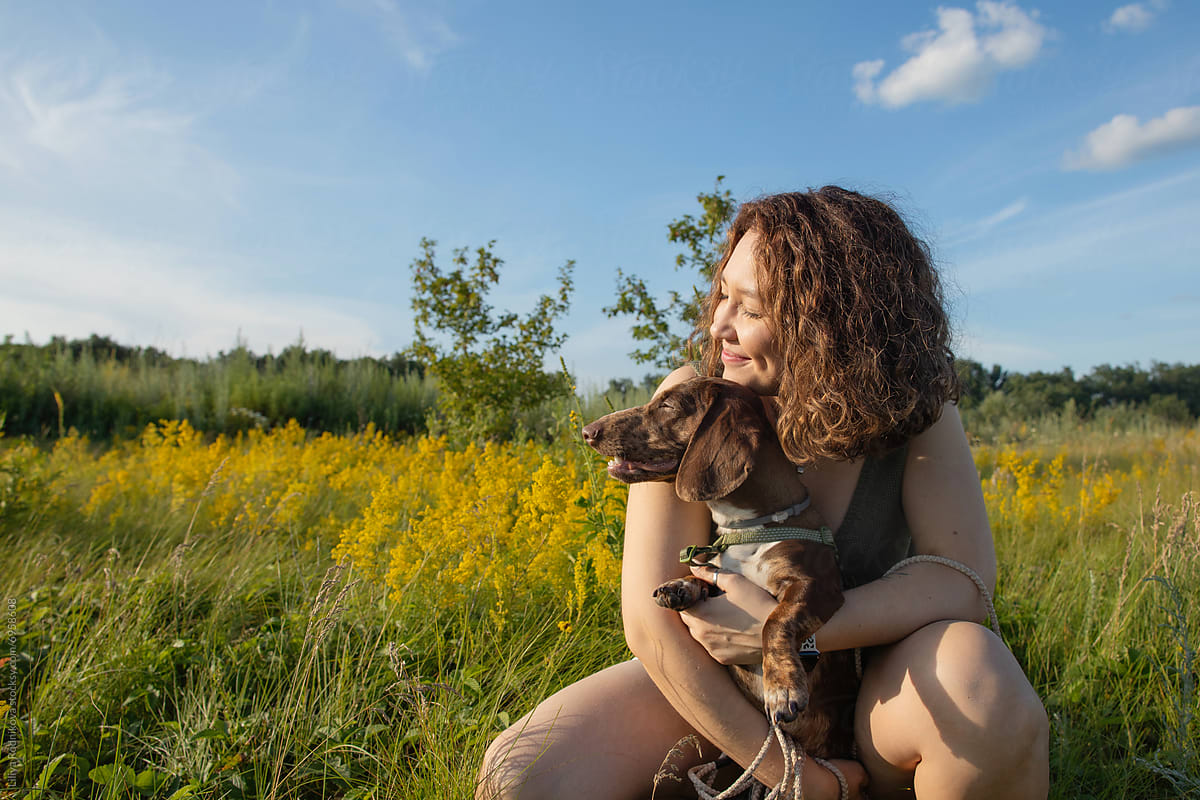 Woman sitting with her dog in a sunny wildflower field
