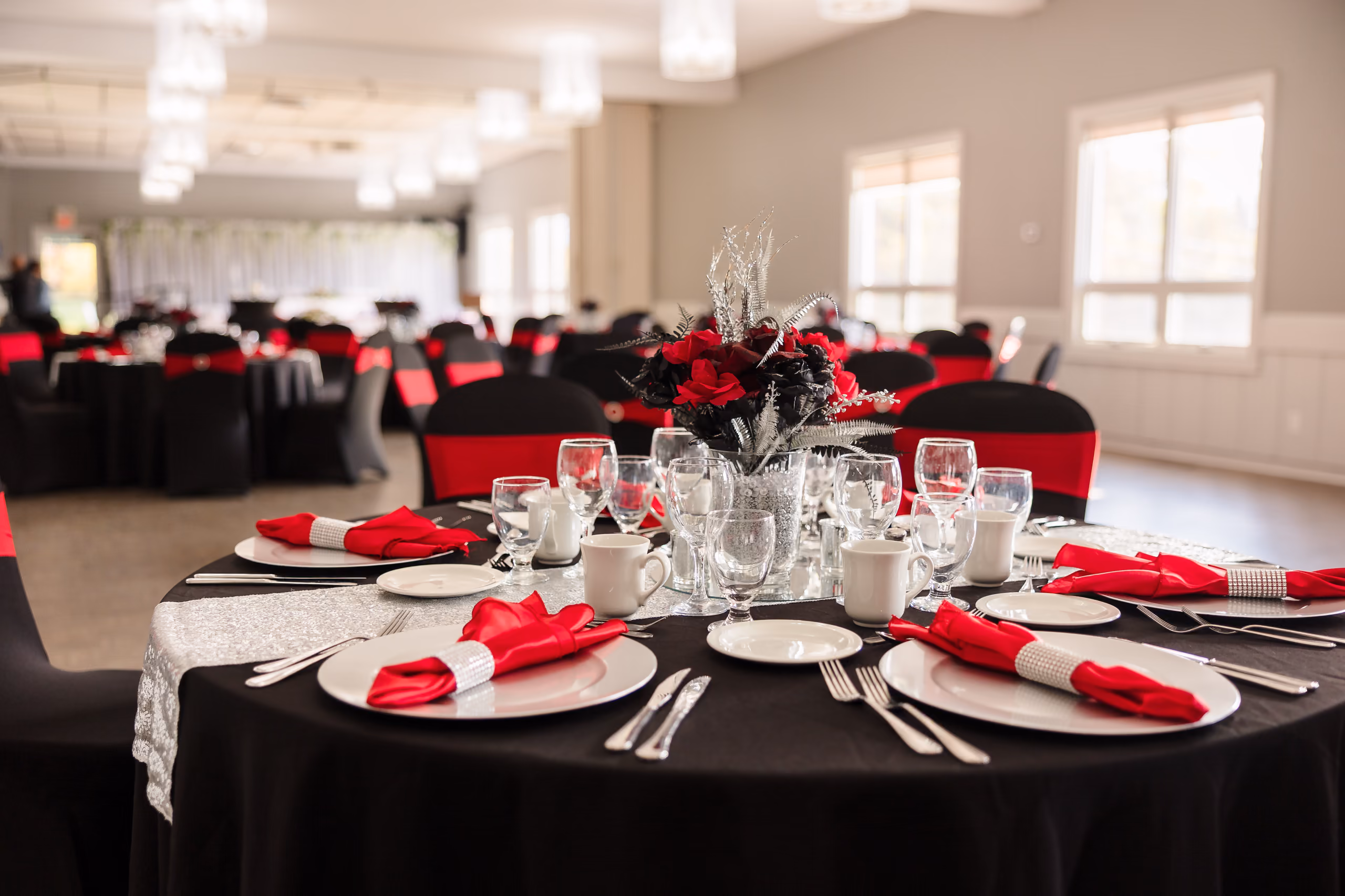 Elegant banquet hall with round tables, black tablecloths, red napkins, and floral centerpieces.