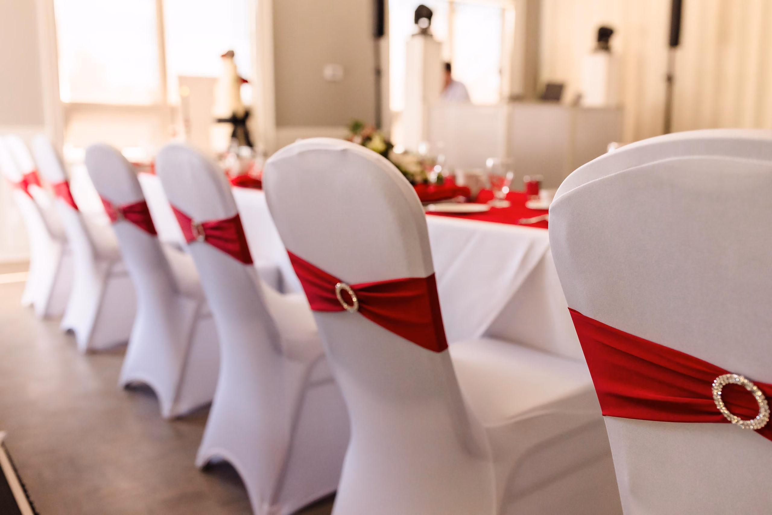 White chairs with red sashes and rhinestone buckles lined up along a decorated banquet table.