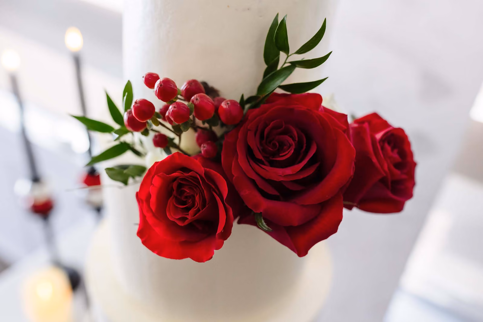 Three red roses and red berries with green leaves on a white cake layer.