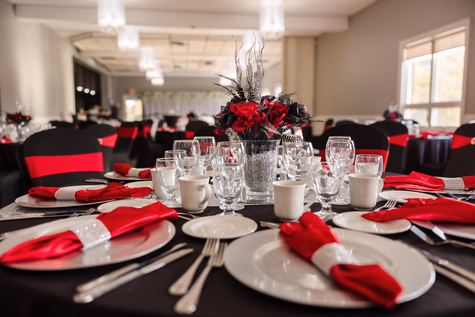 Elegant banquet table with black tablecloth, red napkins, white plates, and a floral centerpiece.