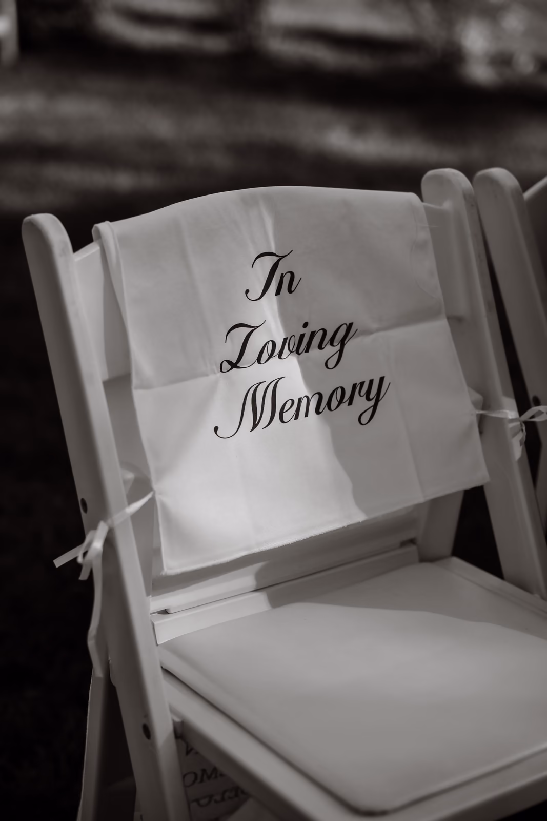 White chair with a cloth reading 'In Loving Memory' draped over its back.