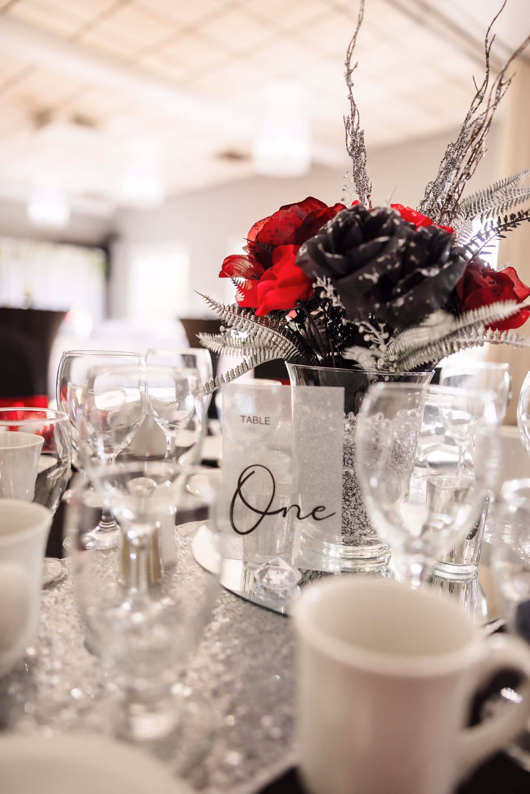 Table set for event with red and black floral centerpiece and a card reading 'Table One'.