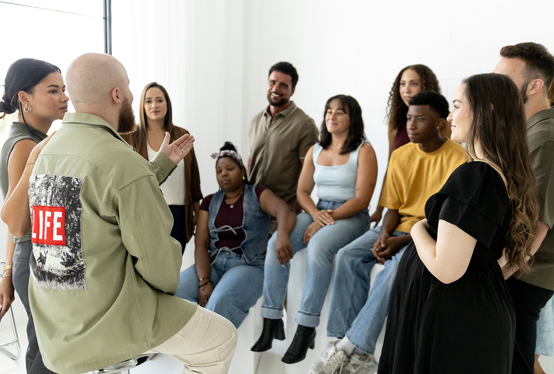 Diverse group in casual wear engaged in conversation in a bright, white room.