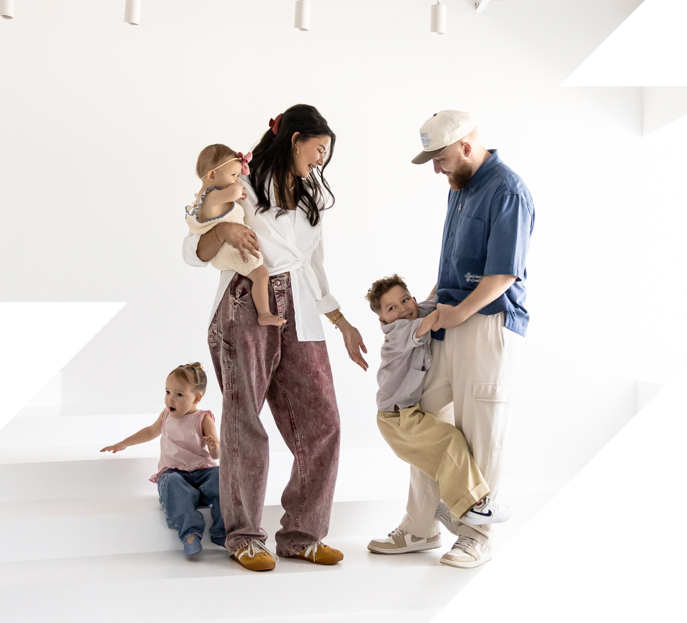 Smiling family with mother holding baby, father playing with son, and daughter sitting on stairs.