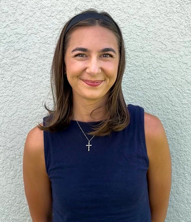 Smiling woman with shoulder-length brown hair wearing a navy sleeveless top and cross necklace.