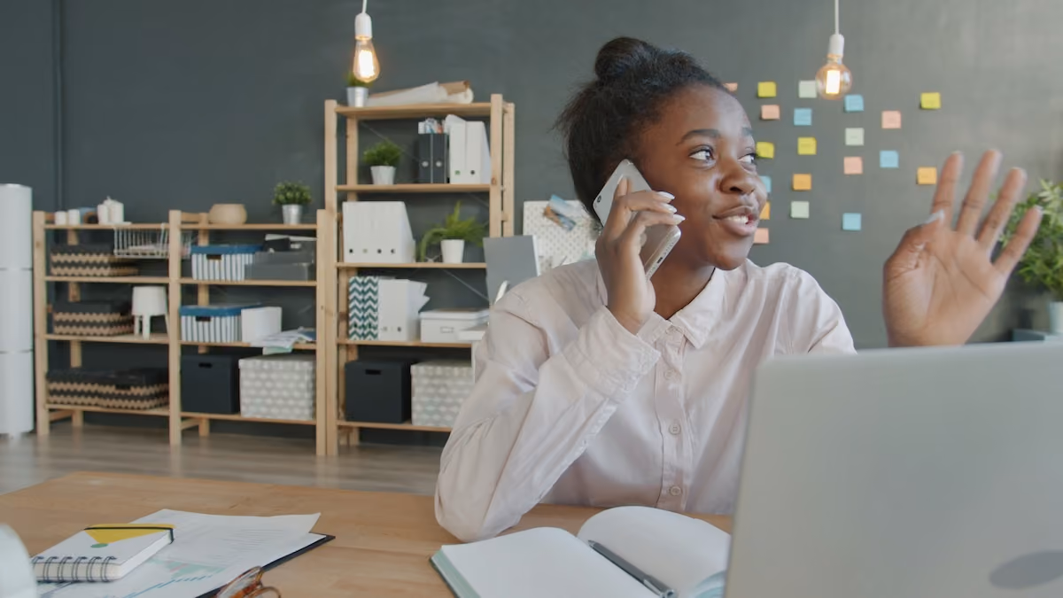 A smiling woman in a white shirt talks on the phone and waves cheerfully while sitting at her desk, reflecting SummitView Holdings' welcoming approach to new inquiries.