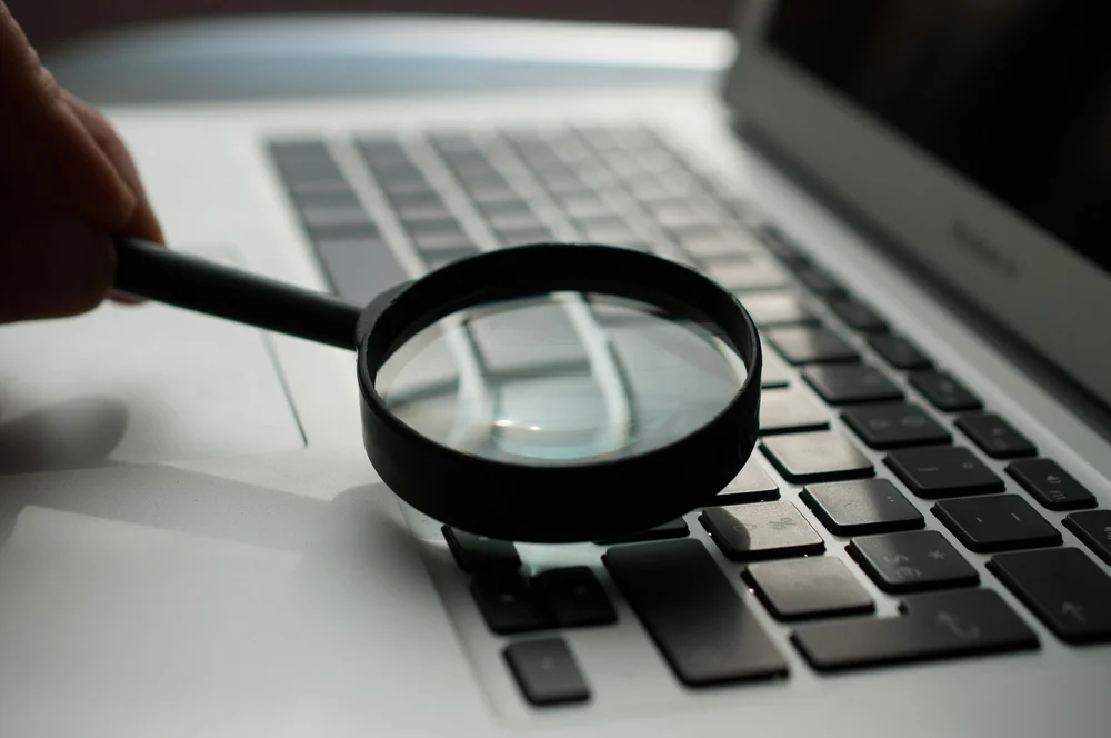 Close-up of a hand holding a magnifying glass over a laptop keyboard, symbolizing SummitView Holdings' close analysis of franchise market data.
