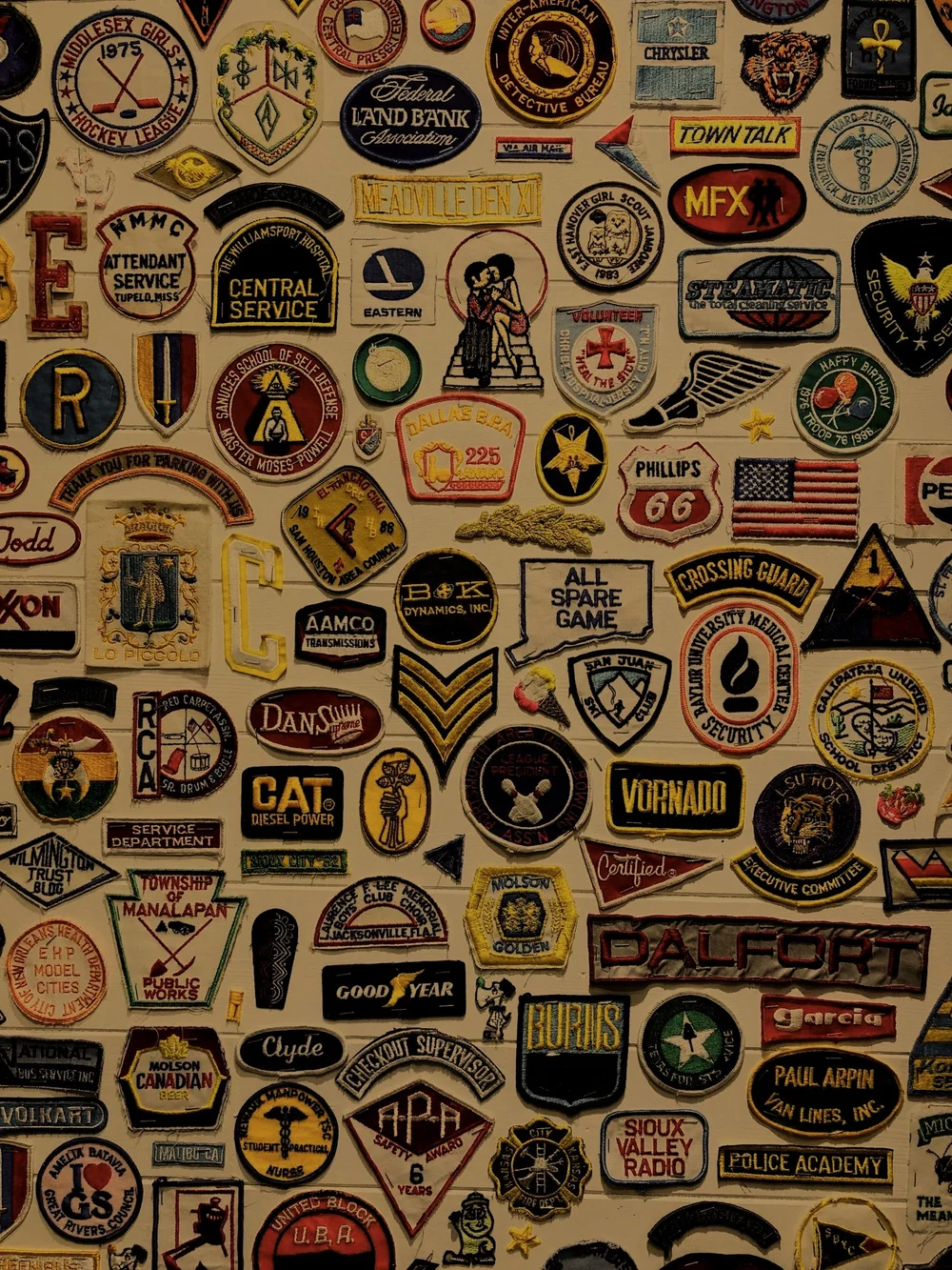 Wall covered in dozens of vintage embroidered patches and emblems, symbolizing the many franchise brands SummitView Holdings can scale across markets.