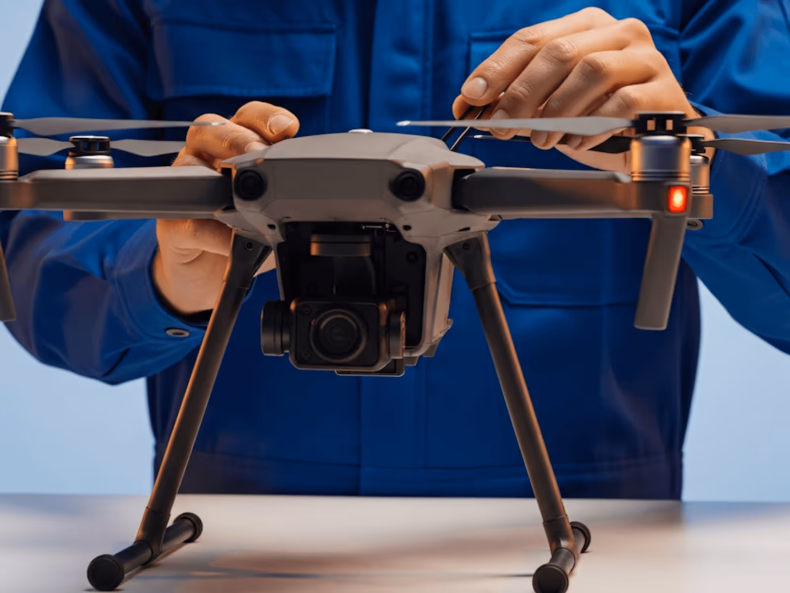 Person in blue shirt adjusting the propeller of a gray quadcopter drone on a table.