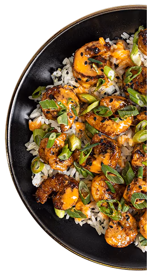 Black bowl with grilled shrimp, white rice, orange sauce, green onions, and black sesame seeds.