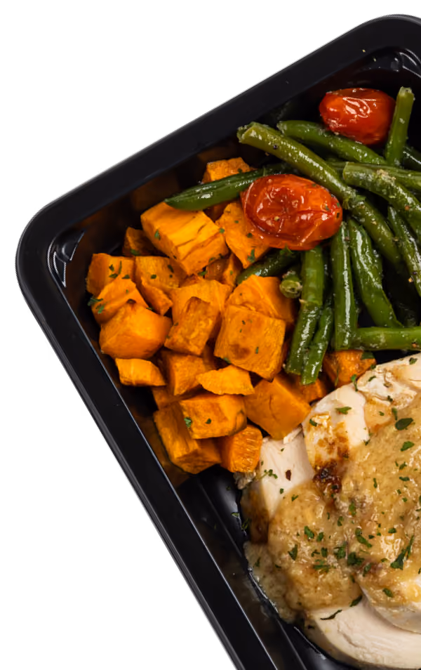 Meal prep container with cooked sweet potato cubes, green beans, cherry tomatoes, and sliced chicken breast with sauce.