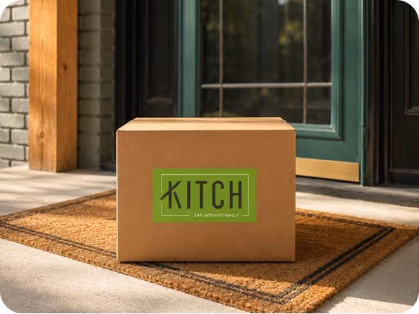 Closed cardboard box labeled Kitch on a brown doormat outside a green door.