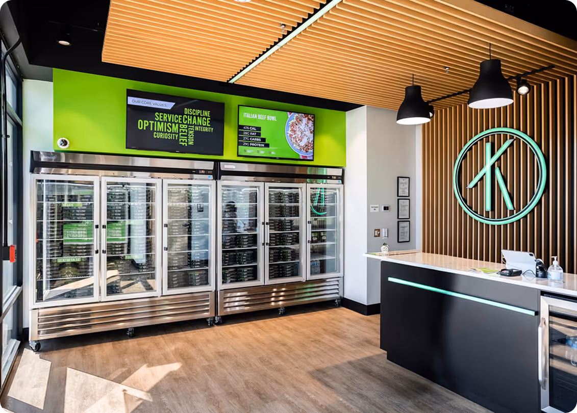 Modern store interior with glass door refrigerators, green accent wall, and black counter with logo behind it.