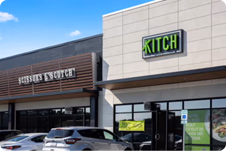 Storefronts of Kitch restaurant with parked cars outside under blue sky.