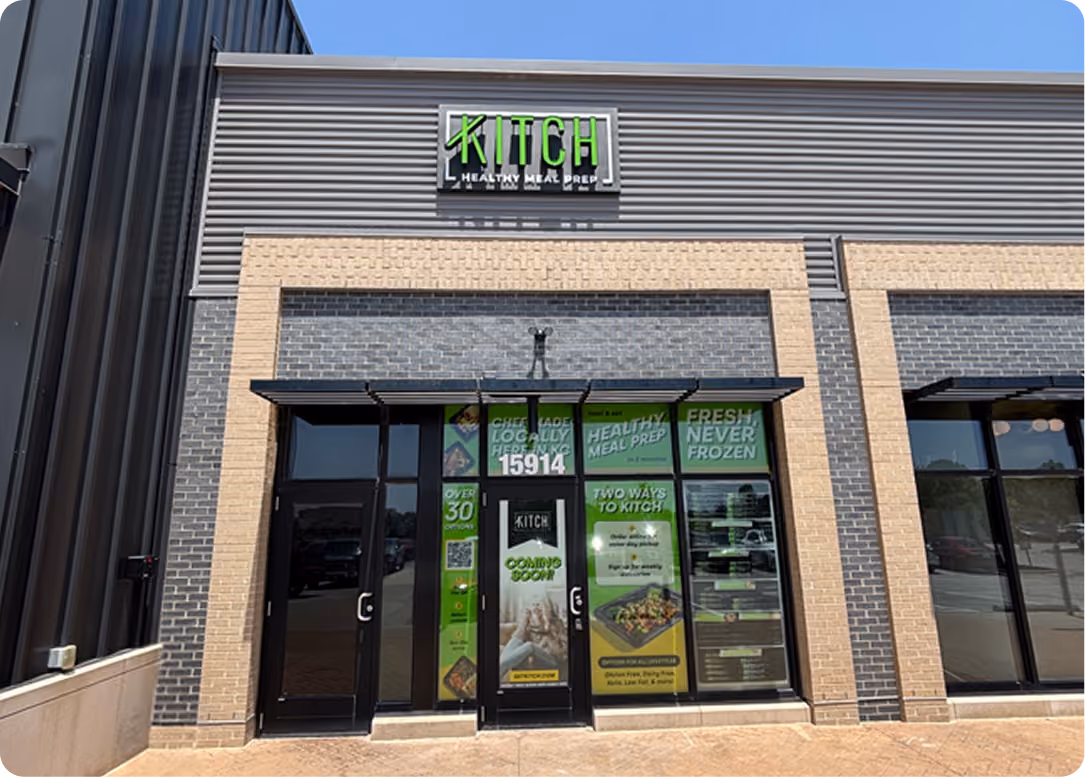 Storefront with KITCH Healthy Meal Prep logo and promotional posters on glass doors and windows.
