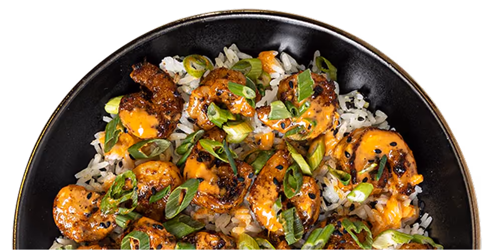 Black bowl with rice, grilled shrimp topped with orange sauce and chopped green onions.