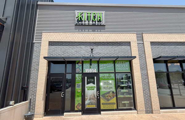 Exterior of Kitch Healthy Meal Prep storefront with promotional posters and glass doors.