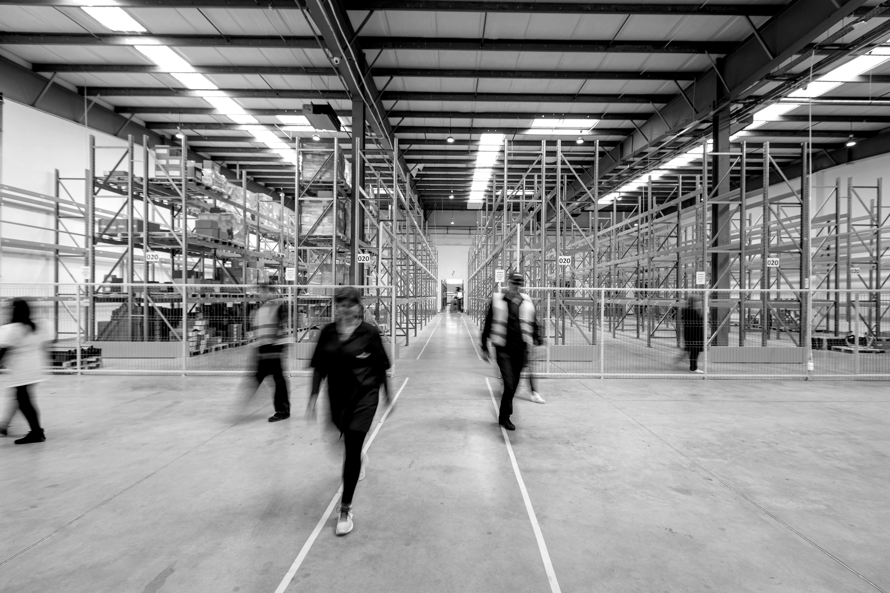 Warehouse staff crossing a large distribution center floor between rows of racking