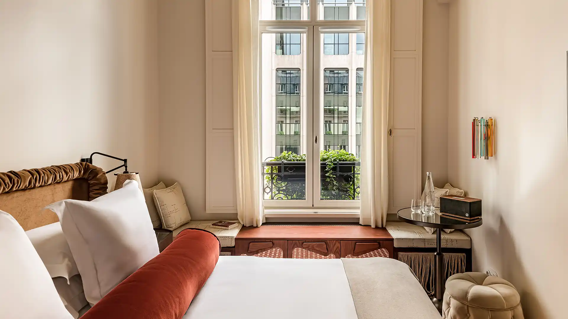 Chambre avec grande fenêtre à balcon fleuri vue sur immeubles parisiens et coussin bolster terracotta Château des Fleurs