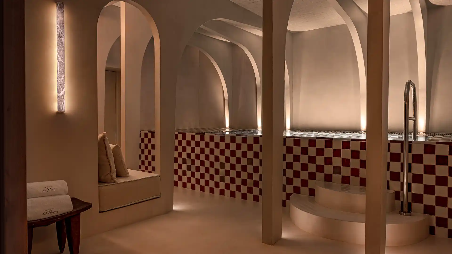 Vue générale du hammam voûté aux arches carrelage à damier rouge et blanc et banquettes coussins spa Château des Fleurs