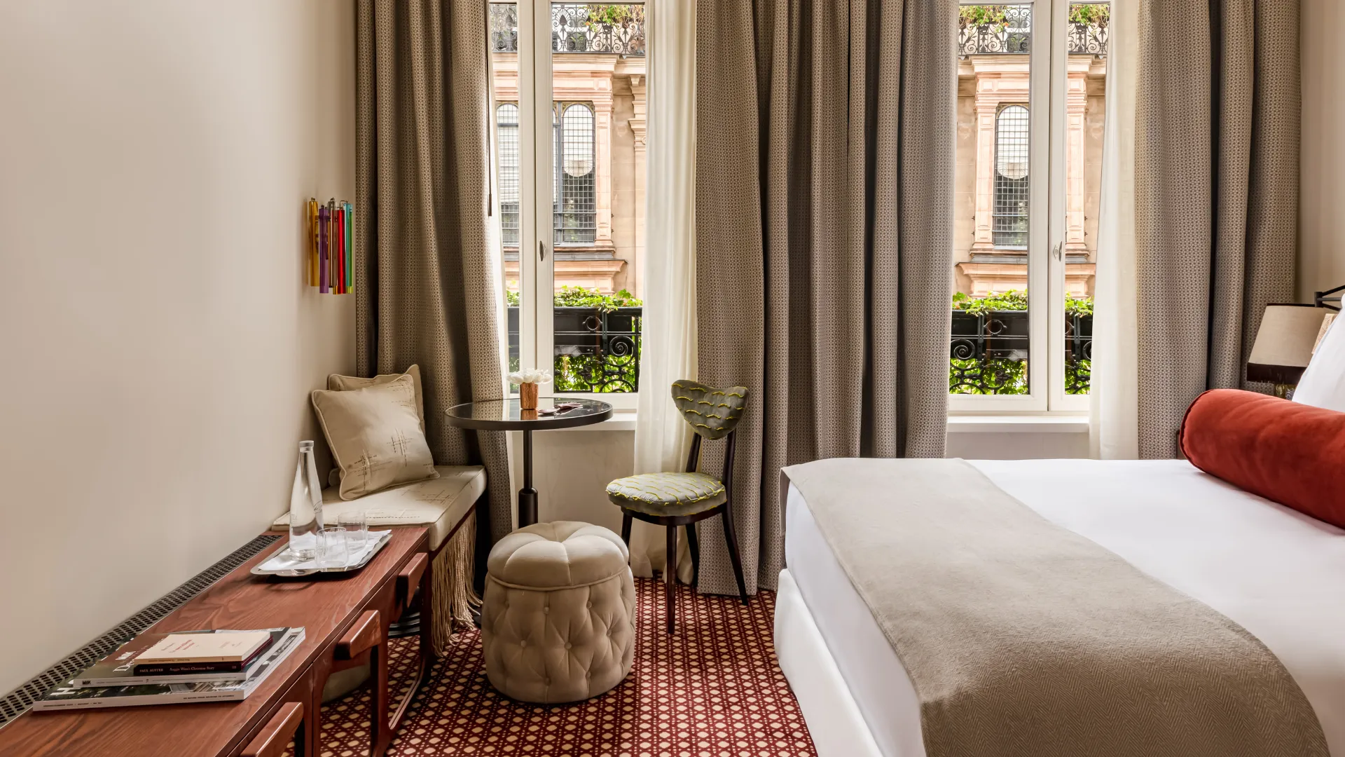 Chambre chaleureuse avec tapis à motifs rouges et vue sur façade haussmannienne Château des Fleurs