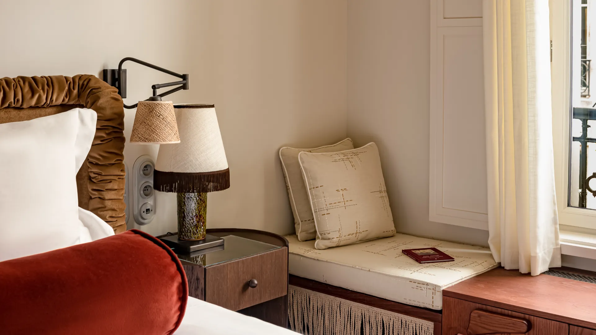 Coin fenêtre avec banquette à franges coussins beige table de chevet et lit velours coussin rouge Château des Fleurs