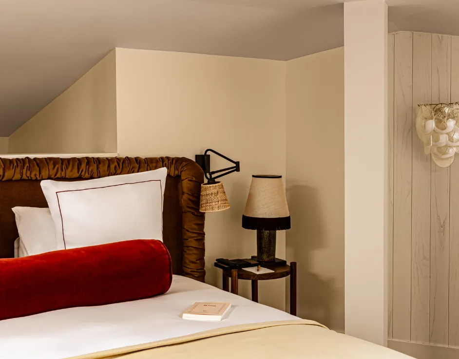 Chambre mansardée avec tête de lit velours coussin rouge et applique florale sculpturale sous plafond en pente Château des Fleurs
