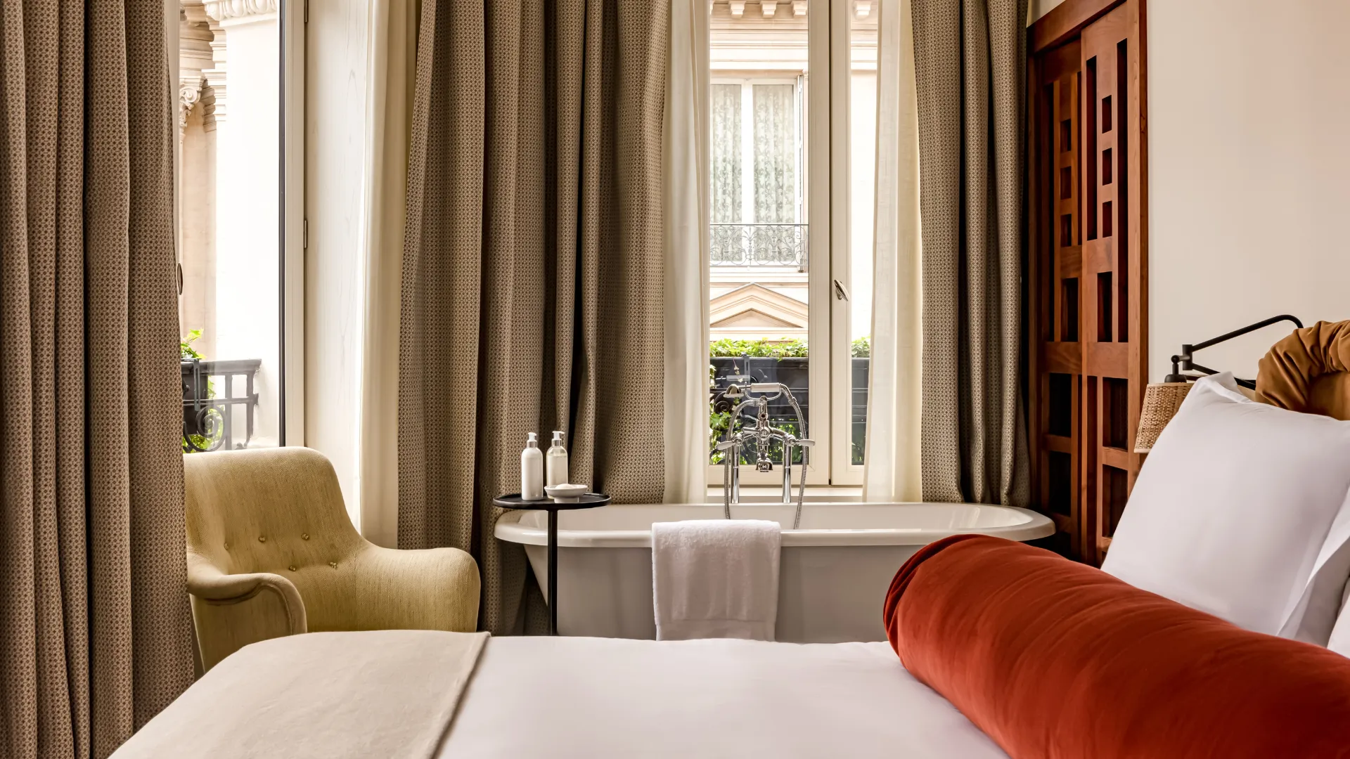 Chambre avec baignoire îlot devant fenêtre et vue sur immeuble parisien fauteuil moutarde Château des Fleurs