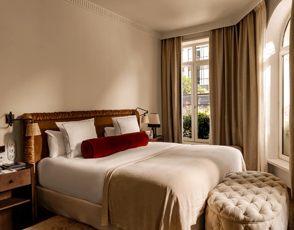 Chambre lumineuse avec lit tête de lit velours coussin bolster rouge et pouf capitonné devant fenêtre Château des Fleurs