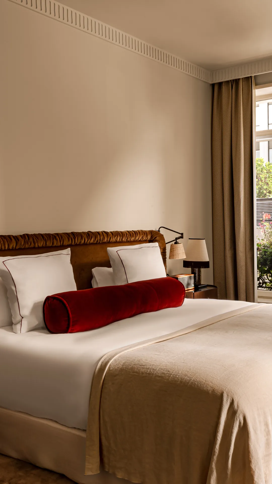 Chambre lumineuse avec lit tête de lit velours coussin bolster rouge et pouf capitonné devant fenêtre Château des Fleurs