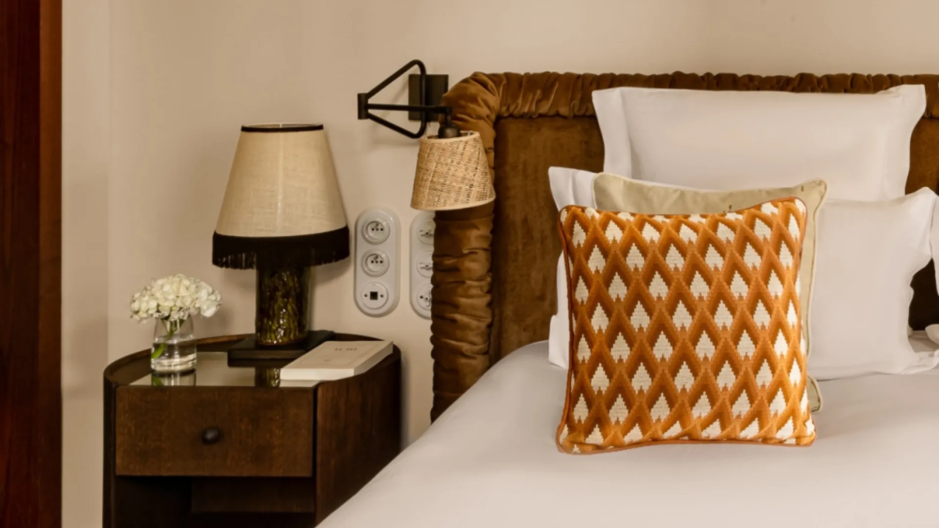 Coin lit avec coussin motif géométrique orange table de chevet et lampes chambre Château des Fleurs