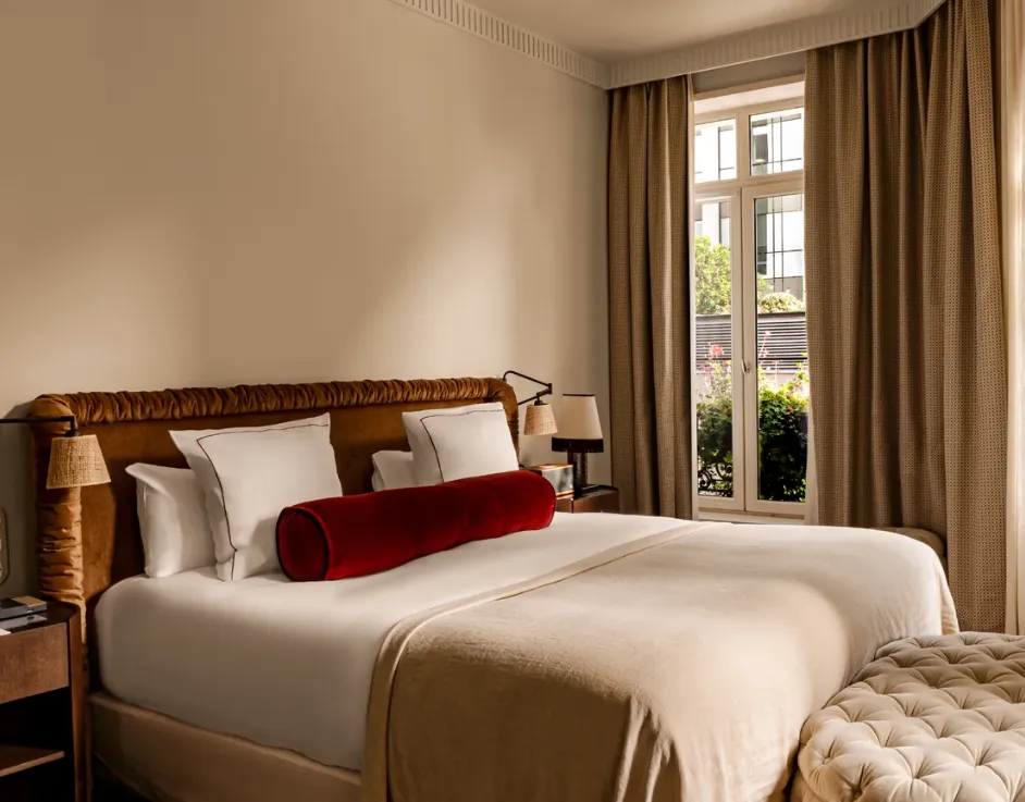 Chambre lumineuse avec lit tête de lit velours coussin bolster rouge et pouf capitonné devant fenêtre Château des Fleurs