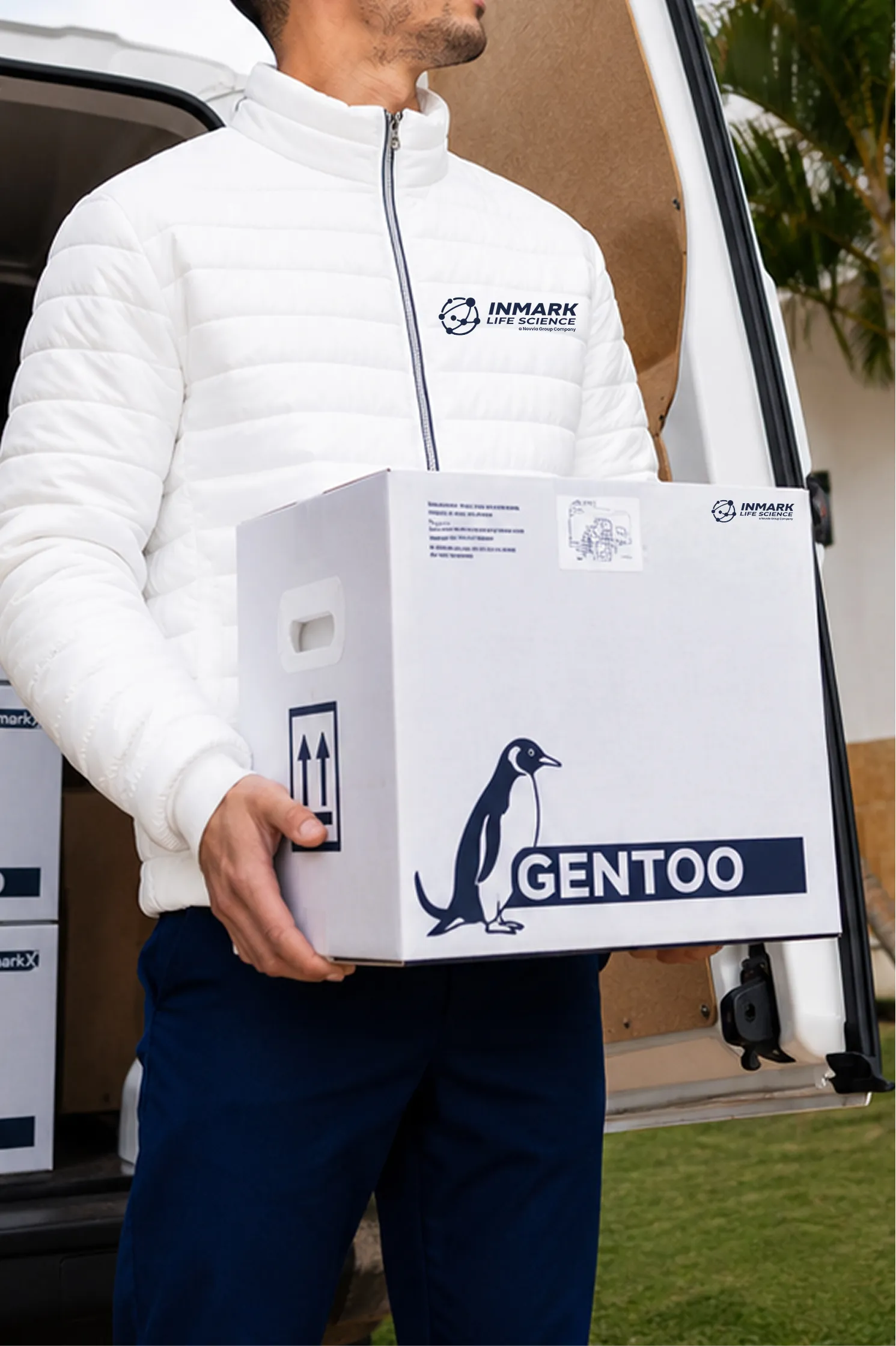 Man wearing a mask and gloves carrying a Gentoo-branded box from a delivery van outdoors.