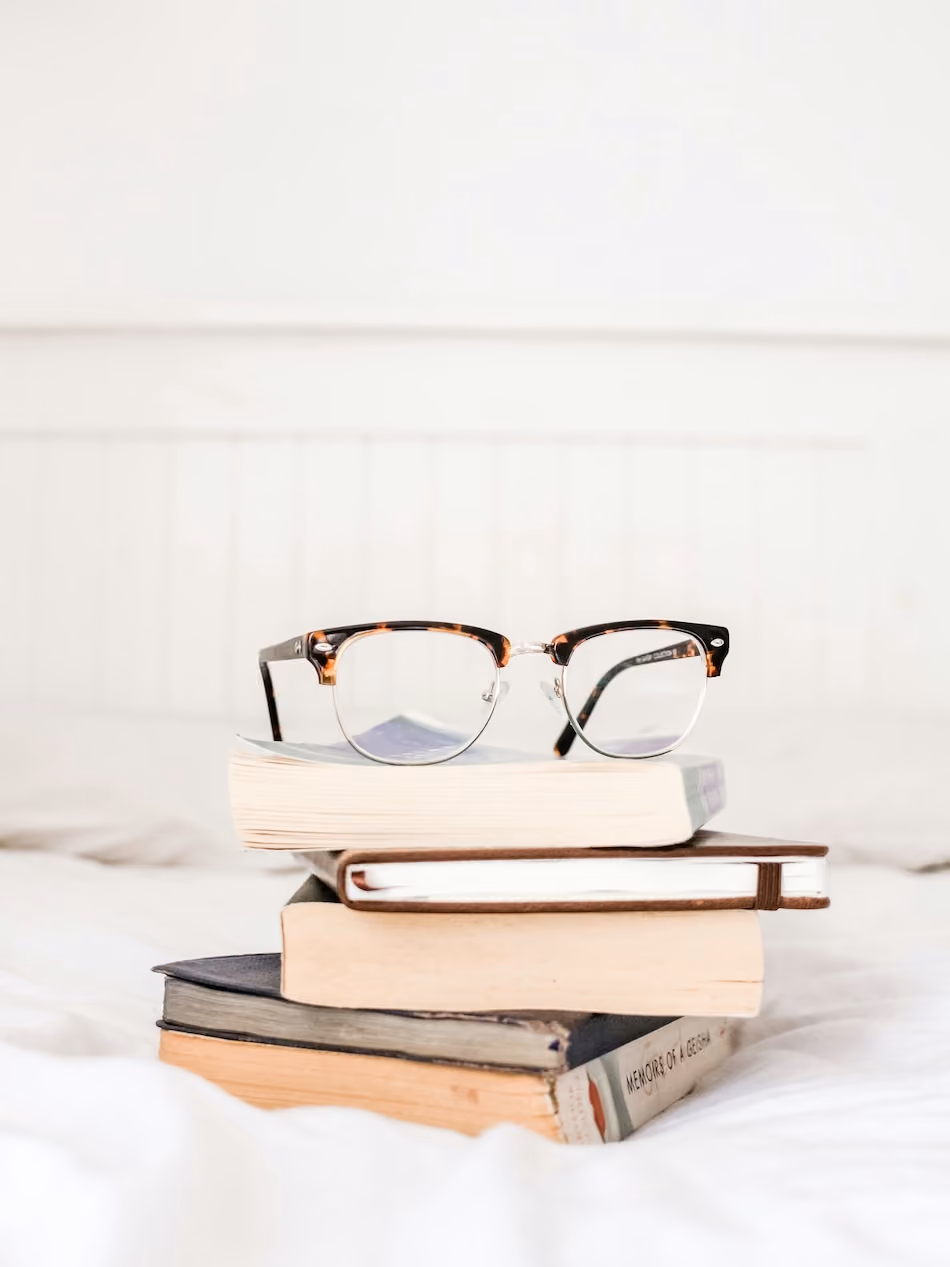 A pair of glasses is placed upside down on top of a stack of books.